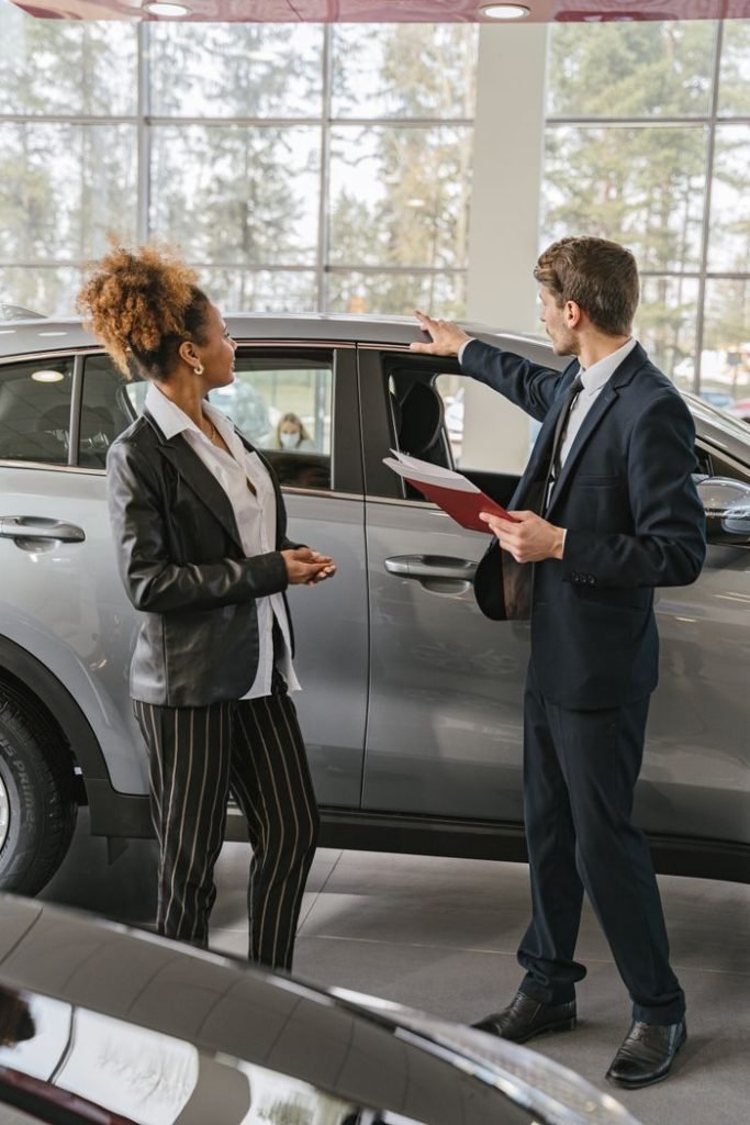 a-woman-buying-a-car-7144225 A woman and a car salesman discuss vehicle options inside a dealership.