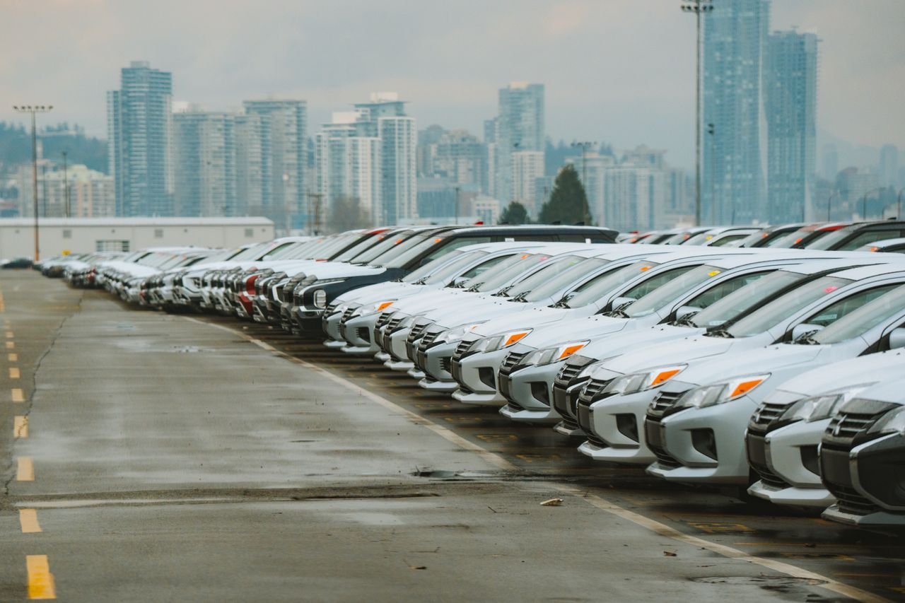 services-01 White cars lined up in a parking lot with a city skyline backdrop.